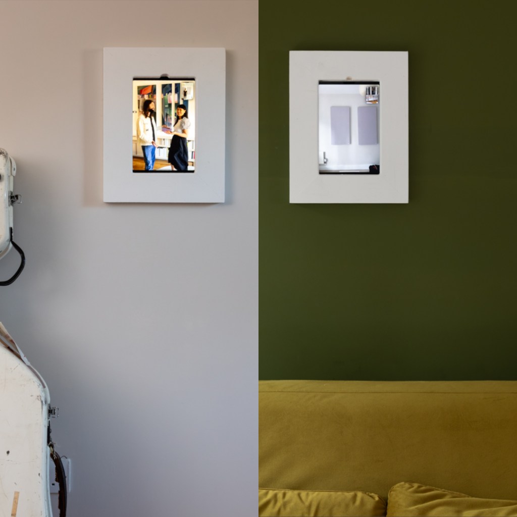 A divided wall with two framed mirrors; the left mirror reflects a scene with two women, while the right mirror shows a plain background with a green wall and a yellow couch below.