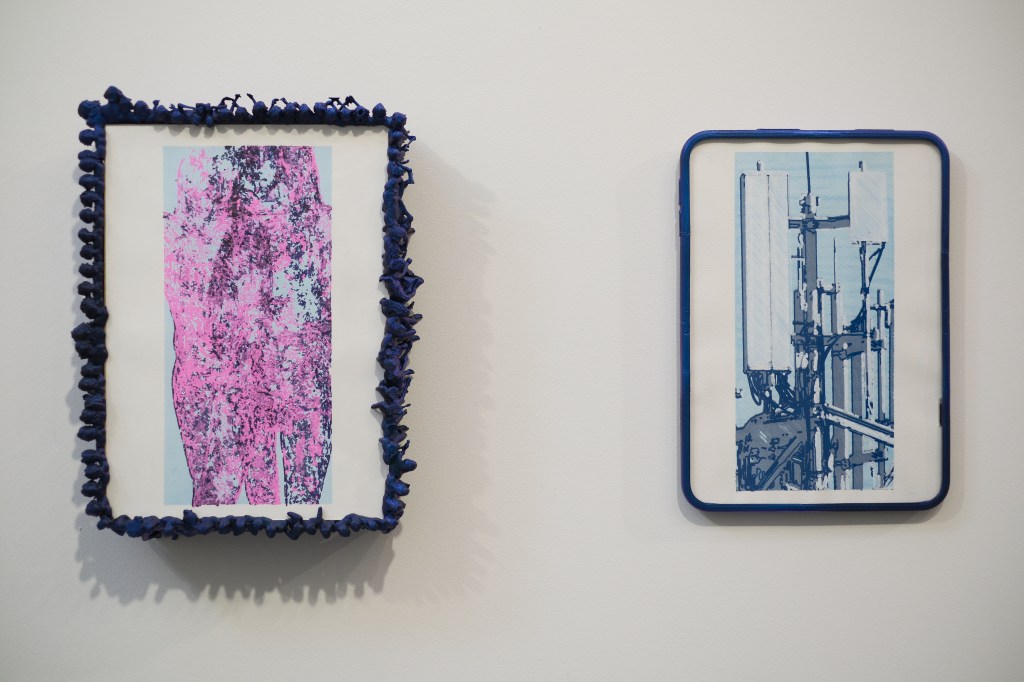 Two framed artworks on a wall; the left piece features vibrant pink textures framed in blue fabric, while the right piece displays a blue-toned graphic of telecommunications equipment.