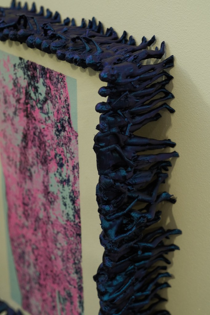 Close-up of a decorative frame designed with intricate figures in vibrant purple and blue hues, surrounding a textured artwork featuring pink and blue tones.